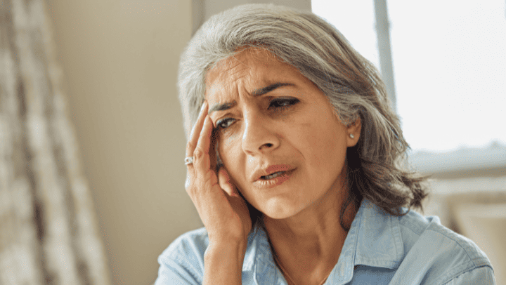 A Senior Lady Holding Her Head In Her Hands And Looking Pained